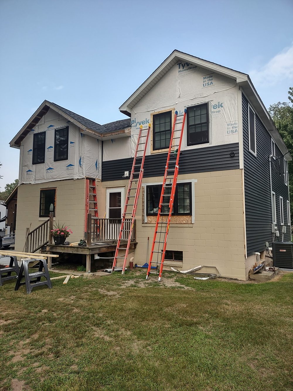 House mid-renovation with Tyvek wrap, partial siding, and ladders in place