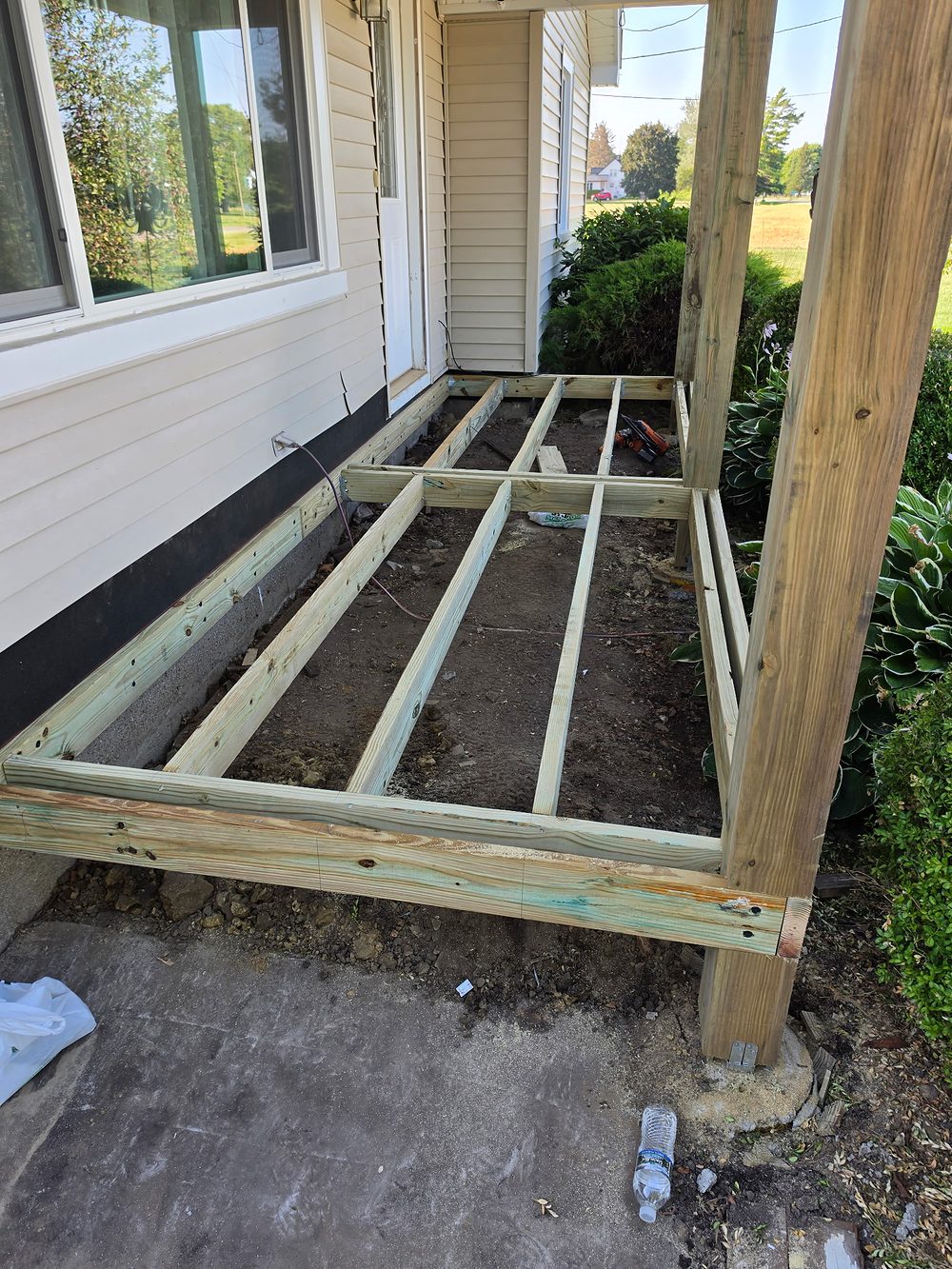 New pressure-treated porch floor framing with ledger, joists and posts against the house foundation