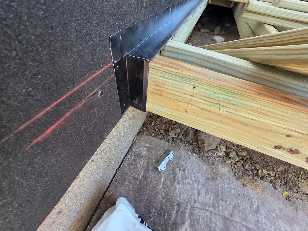 Close-up of new metal ledger flashing with end dam installed over pressure-treated ledger board