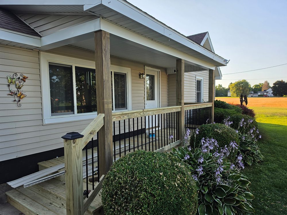 Porch railing installation in progress with black aluminum balusters and new pressure-treated top rail